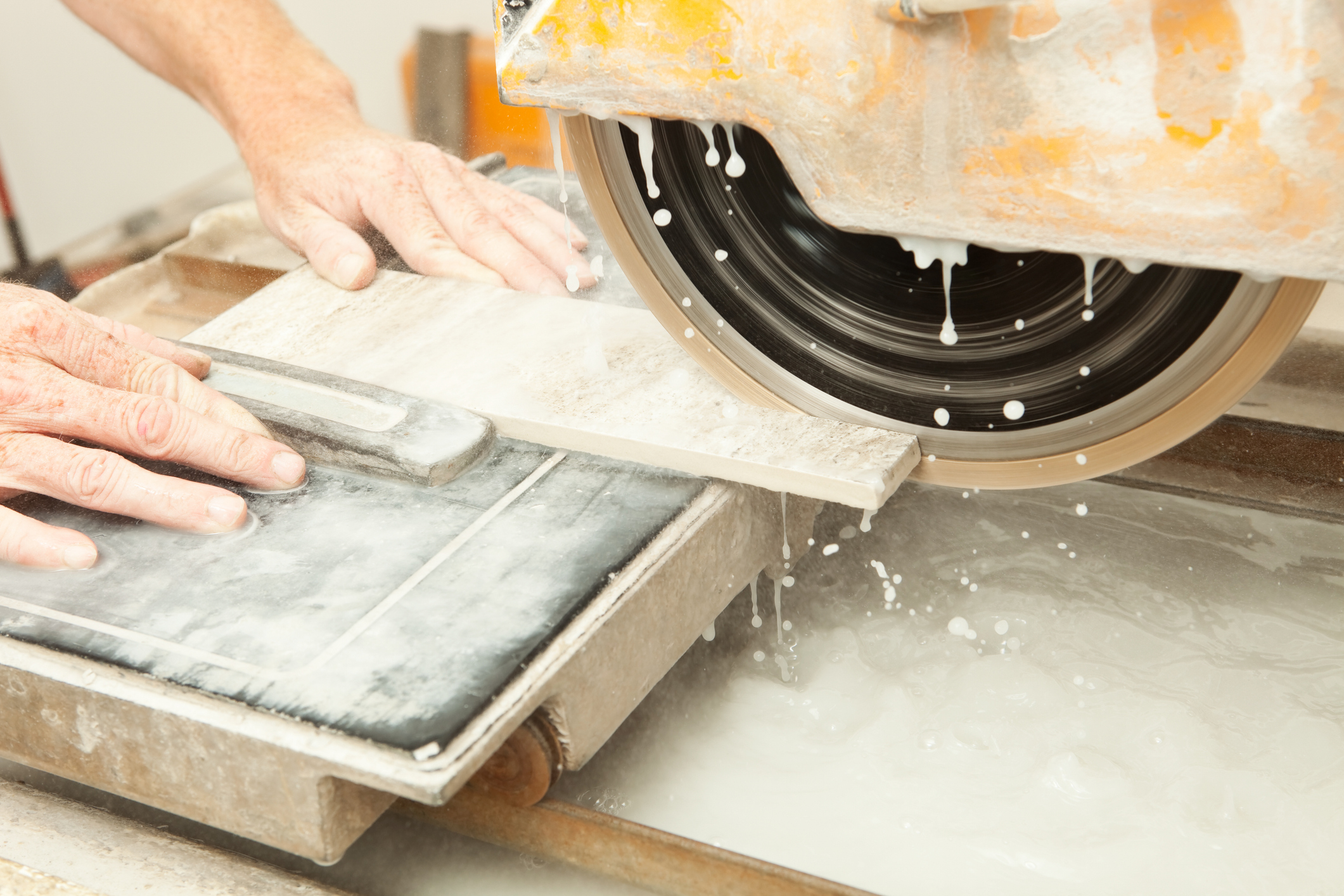 A diamond blade wet saw is being used to cut tile at a house construction site. The water keeps the blade cool and controls dust.